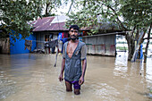 Mirsharai, Bangladesh - 25 August 2024: View of a man standing in floodwaters near his home, the muddy water reflecting the overcast sky, highlighting the distress and resilience of the community.