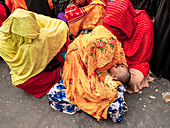 Tongi, Bangladesh - 02 February 2025: View of women in vibrant yellow, orange, and red shawls gathered closely, one cradling a baby in her lap.