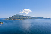 Luftaufnahme der Insel unter strahlend blauem Himmel und einer einzelnen weißen Wolke, die sich auf dem ruhigen blauen Wasser spiegelt, Takawiri Island, Homa Bay, Kenia.