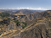 Luftaufnahme der trockenen, sonnenverbrannten Hänge, die auf ein grünes Tal treffen, in dem uralte Steine in der Nähe des Garni-Tempels liegen, Garni, Provinz Kotayk, Armenien.