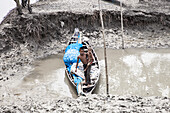 Shyamnagar, Bangladesch - 13. Mai 2023: Blick auf zwei Kinder in einem verwitterten Boot am schlammigen Ufer, deren Gesichter inmitten der kargen Landschaft Resilienz widerspiegeln.