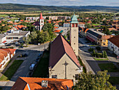 Aerial view of a church with a clock tower stands tall, its steeple reaching towards the sky, a beacon of faith amidst a landscape of vibrant homes, Pukanec, Nitra Region, Slovakia.