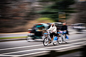 New York, United States - 24 December 2023: View of cyclists speeding along a blurred street near Central Park, the winter trees a muted backdrop to their motion.