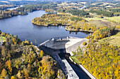 Aerial view of Ottensteiner Stausee dam, a concrete barrier amidst the vibrant autumn foliage, reflecting the clear sky above, Ottenstein, Niederösterreich, Austria.