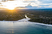 Aerial view of turquoise waters meeting the sandy beach, while the sun sets painting the sky with golden hues over the lush landscape, Diani Beach, Kwale County, Kenya.