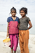 Cox's Bazar, Bangladesh - 01 January 2000: View of two young girls standing on the sandy shore with the tranquil, azure sea stretching out behind them.