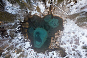 Aerial view of the Geyser Lake's vibrant turquoise waters swirling amidst the snowy taiga forest, Gorno-Altaysk, Altai Republic, Russia.