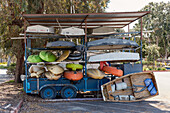 Blick auf gestapelte bunte Kajaks und kleine Boote, die auf einem blauen Anhänger unter einem Wellblechdach sitzen und Schatten auf den Boden werfen, Marina del Rey, Kalifornien, Vereinigte Staaten.