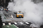 New York, United States - 24 December 2023: View of a yellow taxi emerges from the swirling steam, its bright color a stark contrast against the muted cityscape.