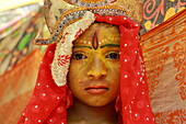 Sitakund, Bangladesh - 21 February 2020: View of a young face adorned with vibrant yellow paint and a crown, framed by a vivid red veil, evokes a sense of ancient tradition and youthful solemnity.