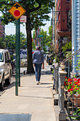 Brooklyn, United States - 13 August 2025: View of a pedestrian strolling along a sun-drenched sidewalk lined with brownstones and lush greenery.