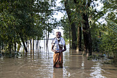 Mirsharai, Bangladesh - 25 August 2024: View of a man standing waist-deep in floodwaters, surrounded by trees, reflecting the stark reality of environmental challenges.