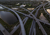 Luftaufnahme des verschlungenen Sägegras-Highway-Kreuzes, in dem sich der Himmel spiegelt, mit Wasserkörpern, in denen sich der Sonnenuntergang widerspiegelt und die einen Teppich aus Licht und Schatten bilden, Sunrise, Florida, Vereinigte Staaten.