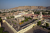Aerial view of buildings and yellow school buses contrasting against the backdrop of a distant hill, Jaipur, Rajasthan, India.
