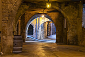View of aged stone arches framing the cobblestone path and inviting passage, illuminated by warm lights in Villefranche-sur-Mer, Provence-Alpes-Côte d'Azur, France.