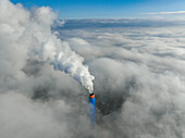 Aerial view of a tall smokestack piercing through a sea of fluffy clouds, its vibrant blue and orange contrasting with the soft, ethereal white, Torino, Piemonte, Italy.