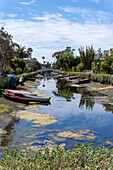 View of boats resting on the tranquil canal reflecting the sky, crossed by a bridge and framed by lush greenery, Los Angeles, California, United States.