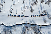 Aerial view of several vehicles lined up on a snow-covered landscape, contrasting the stark white with the dark vegetation, Sakha Republic, Russia.