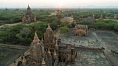 Aerial view of ancient temples and pagodas dot the landscape under the golden hues of sunrise, creating a mystical scene, Old Bagan, Mandalay Region, Myanmar.