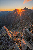 Aerial view of the sun bursting over rugged mountain peaks, casting long shadows across the rocky terrain, Vysoké Tatry, Prešov Region, Slovakia.
