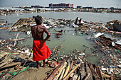 Chattogram, Bangladesh - 25 October 2022: View of a man in a red garment standing amidst debris-filled water, a stark reminder of nature's raw power.