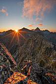 Aerial view of the sun ablaze over rugged peaks, casting long shadows across the dramatic landscape of Vysoké Tatry, Prešov Region, Slovakia.