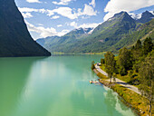 Luftaufnahme des türkisfarbenen Sees, in dem sich die dramatische Berglandschaft unter einem strahlend blauen Himmel spiegelt, Oldevatnet, Vestland, Norwegen.