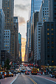New York, United States - 11 July 2025: View of the vibrant cityscape, where towering skyscrapers meet bustling streets alive with cars and pedestrians, all bathed in the warm glow of the setting sun.