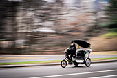 New York, United States - 24 December 2023: View of a pedicab speeds along the road, its blurred motion contrasting with the stark, winter trees and the distant buildings.