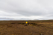 View of a solitary figure in a yellow jacket perched on a rock amidst the vast, earthy landscape under a brooding sky, Vik, Iceland.