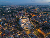 Aerial view of the illuminated Altare della Patria standing majestically amid the ancient cityscape, its white marble contrasting against the darkening sky, Roma, Lazio, Italy.