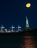 View of the Statue of Liberty stands majestically against the dark sky, illuminated by a full moon, with city lights twinkling in the background, New York, New York, United States.