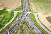 Aerial view of converging railway lines slicing through a vibrant patchwork of golden fields and verdant meadows, Deutschlandsberg, Styria, Austria.