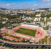 Aerial view of the Givat Ram Stadium nestled amid lush greenery and urban architecture, a vibrant contrast of sports and city life, Jerusalem, Israel.