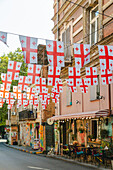View of Georgian flags fluttering above a quaint street with colorful buildings and cozy cafes, creating a vibrant atmosphere, Tbilisi, Tbilisi, Georgia.