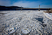 Aerial view of an icy river reflects the cold winter sky, with the Rip Van Winkle Bridge spanning the distance, Hudson, New York, United States.
