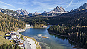 Luftaufnahme des ruhigen, tiefblauen Wassers des Lago di Misurina, in dem sich die hoch aufragenden Gipfel der Drei Zinnen spiegeln, eingebettet in goldene Wälder, Misurina, Belluno, Italien.
