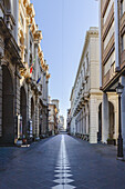 View of quiet street lined with ornate buildings under a clear sky, a white line running down the center, creating a mesmerizing perspective, Chieti, Abruzzo, Italy.