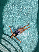 Aerial view of a woman floating serenely in the crystal-clear turquoise water of a swimming pool, ripples dancing in the sunlight, Tambon Sam Roi Yot, Chang Wat Prachuap Khiri Khan, Thailand.