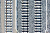 Aerial view of parallel train tracks slicing through a landscape of gray gravel, creating a stark contrast of lines and textures, Deutschlandsberg, Styria, Austria.
