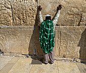 Jerusalem, Israel - 01. November 2019: Blick auf einen Mann beim Gebet an der Klagemauer, die Hände gegen die alten Steine erhoben, ein leuchtend grünes Tuch über die Schultern drapiert.
