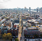 Luftaufnahme von Straßenschluchten, die von Gebäuden gesäumt sind, und einer Parade von New York-Marathon-Läufern, die sich in Richtung der entfernten Skyline von Manhattan strecken, Brooklyn, New York, Vereinigte Staaten.