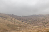Blick auf sanfte Hügel, die in eine schwere Nebeldecke gehüllt sind, die trockene Landschaft ist eine Studie in gedämpften Braun- und Grautönen, Votoran-Pass, Provinz Vayots Dzor, Armenien.