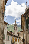 Blick auf alte Gebäude mit verwitterten Mauern, die einen entfernten Kirchturm einrahmen, der den blauen Himmel über den grünen Bergen durchsticht, Scanno, Abruzzen, Italien.