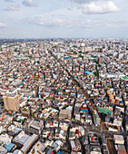 Luftaufnahme von dichten Gebäuden und einer Eisenbahn, die sich unter einem bewölkten Himmel durch die Stadtlandschaft zieht, Tokio, Tokio, Japan.