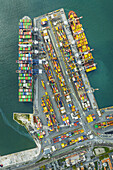 Luftaufnahme des geschäftigen Hafens mit Schiffen, die mit Containern beladen sind, eine Symphonie industrieller Aktivität vor dem Hintergrund des Ligurischen Meeres, Hafen von La Spezia, Ligurien, Italien.