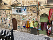 Jerusalem, Israel - 02 November 2019: View of ancient stone walls adorned with vibrant Arabic script and colorful garments hanging outside a shop near the historic streets.
