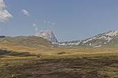 Blick auf sonnenverwöhnte Felder und die imposanten, schneebedeckten Berggipfel unter einem klaren Himmel, eine ruhige Szene der Natur, Isola del Gran Sasso D'italia, Abruzzen, Italien.
