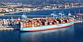Vado Gateway, Italy - 21 September 2025: Aerial view of a vast Maersk container ship dwarfing the port cranes, a vibrant testament to global trade against the coastal cityscape.