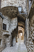 View of the narrow cobblestone street with aged stone buildings and arched passageways, lit by a vintage street lamp, Castelvecchio Calvisio, Abruzzo, Italy.